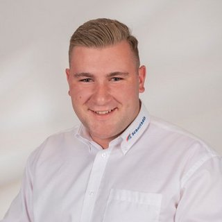 Professionelles Porträt eines lächelnden Mannes in Hemd Ein junger Mann mit kurzem, blondem Haar lächelt freundlich in die Kamera, gekleidet in ein weißes Hemd mit Logo.